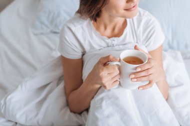Hayalperest bir kadının elinde fincanla yatakta çay tutuşu. 