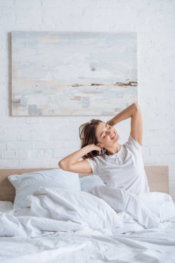 Hayalperest kız yatakta saçlarına dokunurken gülümsüyor. 