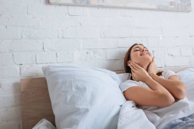 happy woman touching neck while dreaming and lying on bed 