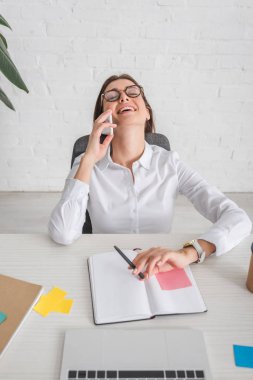 Gözlüklü mutlu iş kadını ofiste akıllı telefonla konuşuyor. 