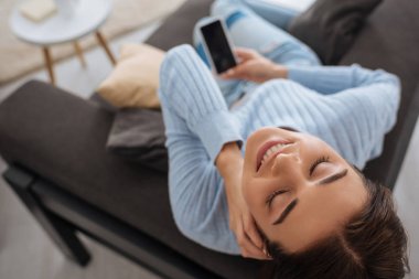 Evinde boş ekranlı akıllı telefonu tutan mutlu kadının üst görüntüsü 