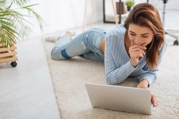 Neşeli Kız Dizüstü Bilgisayar Kullanıyor Evde Halıda Yatarken Gülümsüyor — Stok fotoğraf
