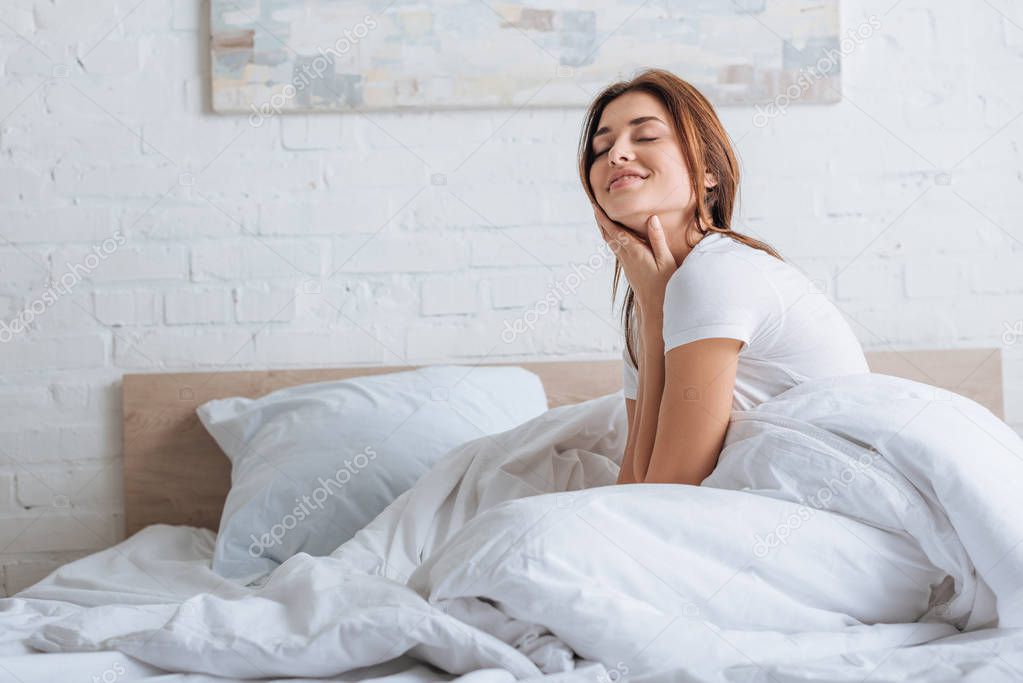dreamy young woman touching neck and resting in bed 