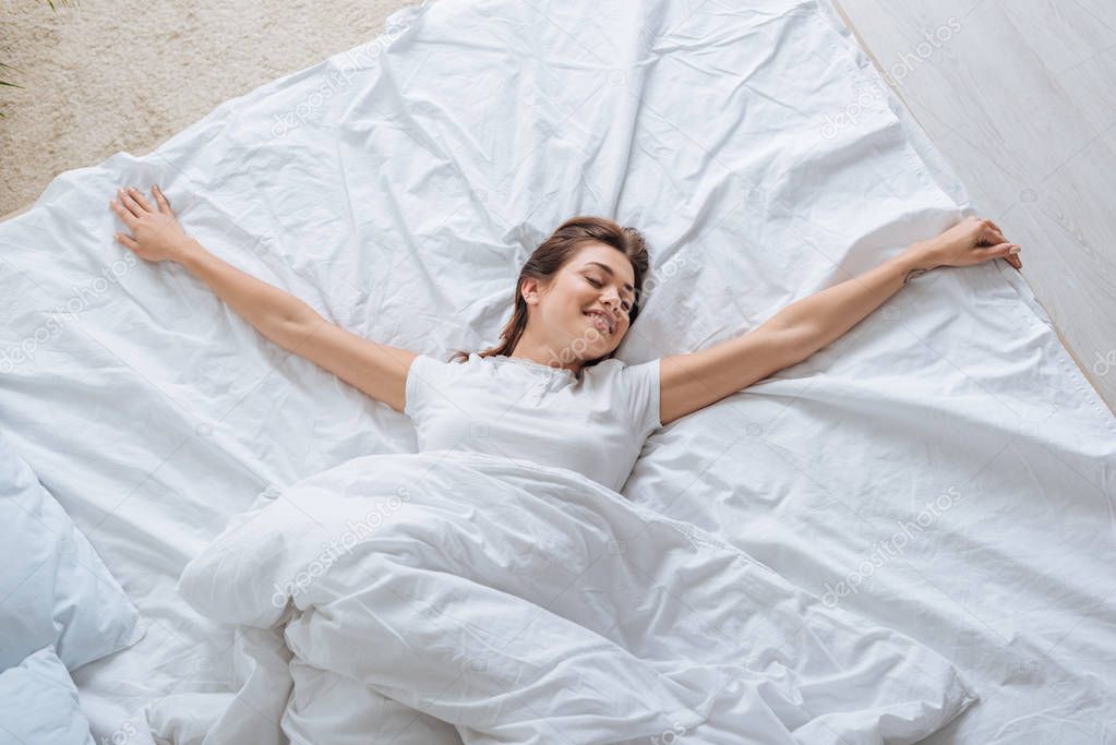 top view of smiling young woman with closed eyes resting in bed 