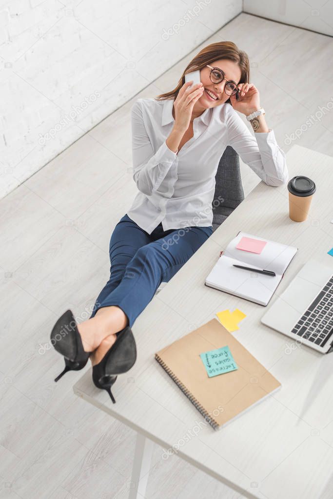 happy businesswoman talking on smartphone and relaxing in office 