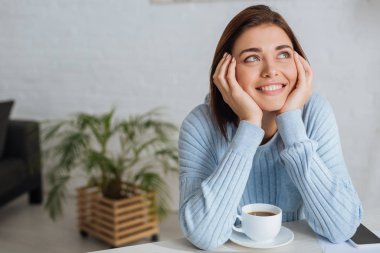 dreamy young woman smiling near cup with coffee  clipart