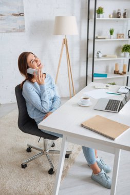 Neşeli genç bir kadın akıllı telefondan konuşuyor ve evde takılıyor. 