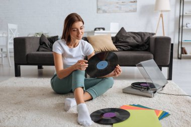 smiling girl holding vinyl record while chilling at home  clipart