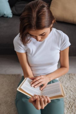 Kanepenin yanındaki halıda oturan kadının kitap okuması 
