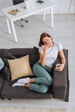 overhead view of tired girl chilling of sofa with cup of tea  clipart