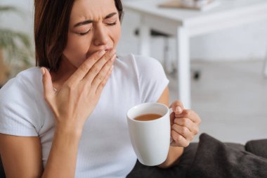 tired woman yawning and cover mouth while holding cup  clipart