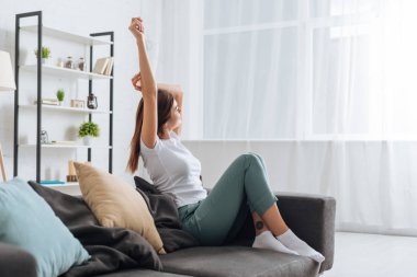 selective focus of young dreamy woman with outstretched hand relaxing in living room  clipart