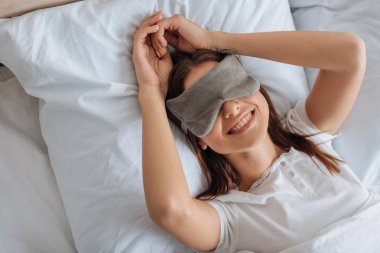 Yatak odasında dinlenen, göz maskeli, pozitif genç bir kadının üst görüntüsü. 