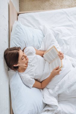 Yatakta dinlenirken kitap okuyan mutlu kız manzarası. 