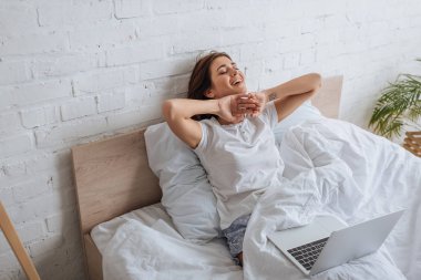 dreamy woman smiling while chilling in bed near laptop   clipart