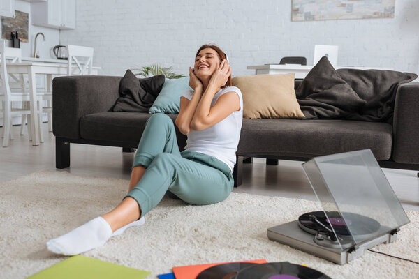 cheerful girl listening music in headphones near vintage record player 