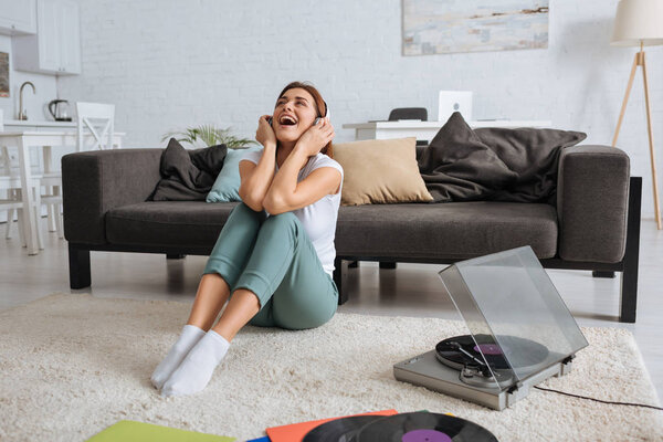 cheerful girl listening music in headphones and singing near vintage record player 