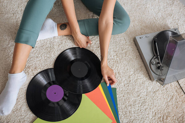 cropped view of tattooed woman sitting near retro vinyl player 