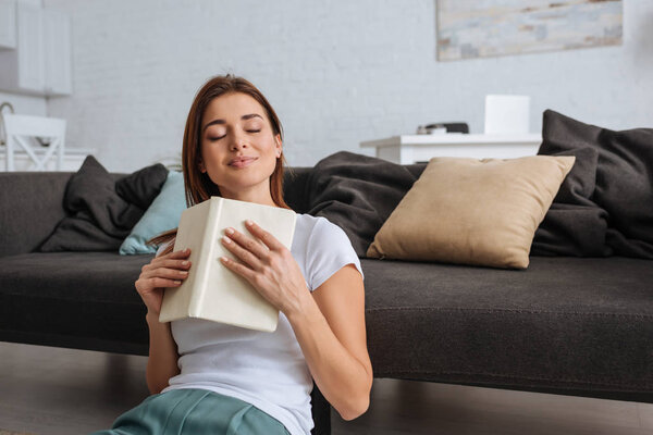 dreamy girl holding book while sitting in living room 