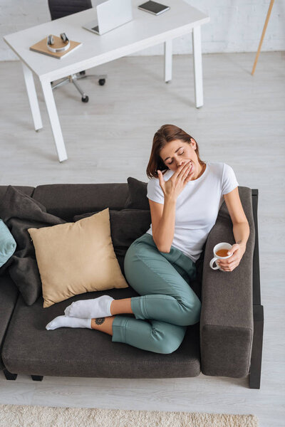 overhead view of tired girl chilling of sofa with cup of tea 