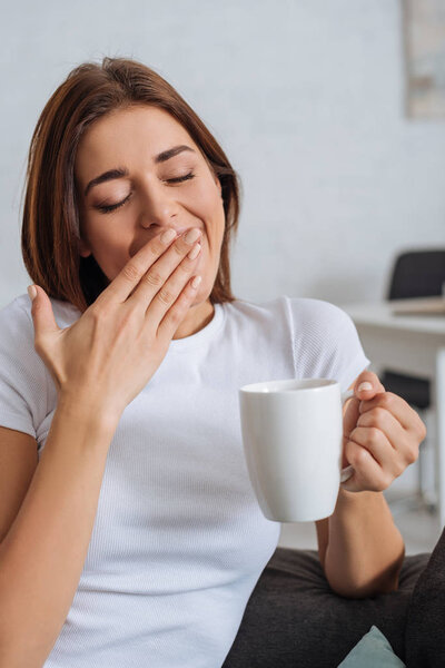 tired girl yawning and cover mouth while holding cup 