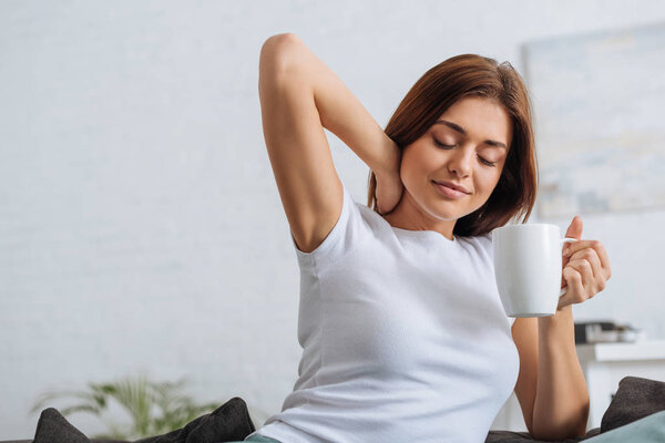 young woman with closed eyes holding cup with tea 