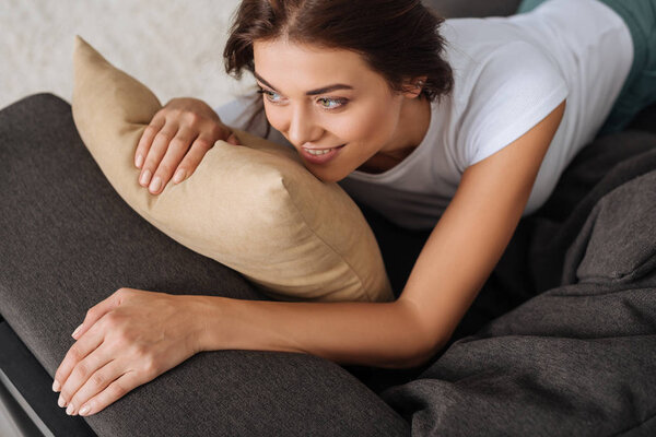 overhead view of smiling woman chilling while lying on sofa near pillow 