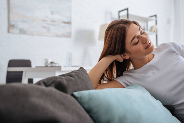 selective focus of dreamy young woman relaxing on sofa at home 