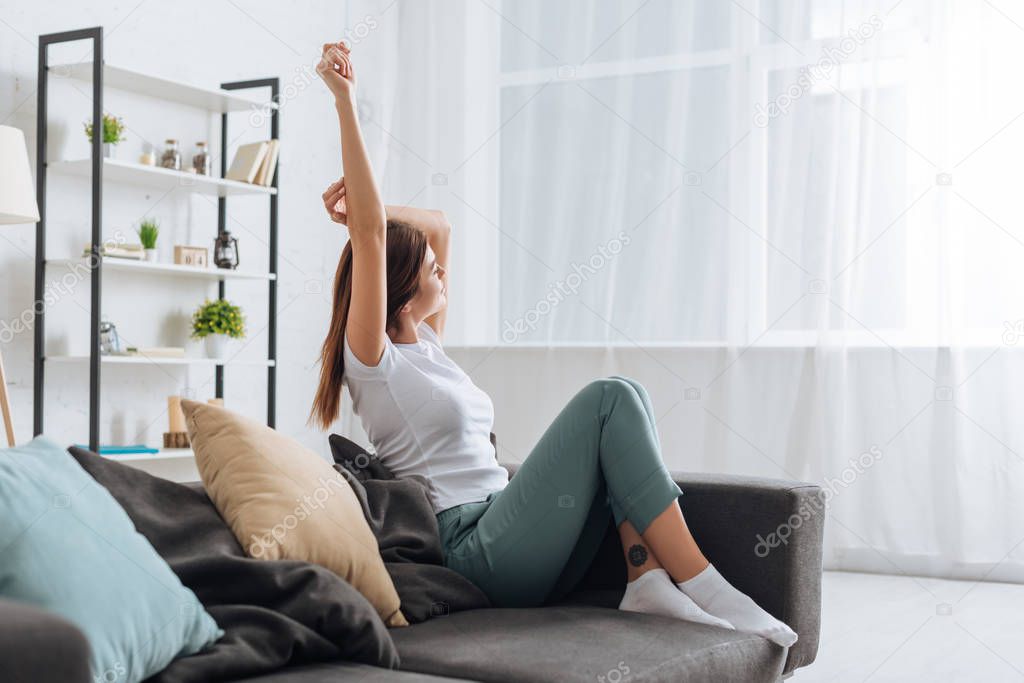 selective focus of young dreamy woman with outstretched hand relaxing in living room 