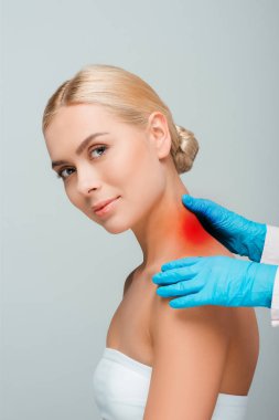 Kırpılmış mavi lateks eldivenli doktor görüşü Gri üzerinde kırmızı lekeli kadının boynuna dokunuyor 