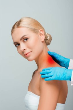 cropped view of doctor in blue latex gloves touching woman neck with red mark isolated on grey  clipart