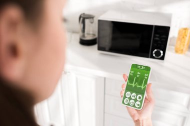 selective focus of woman holding smartphone with health app and microwave on background 