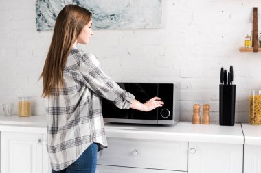 side view of attractive woman using microwave in kitchen 