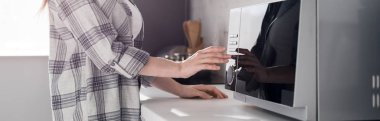 panoramic shot of woman in shirt using microwave in kitchen 