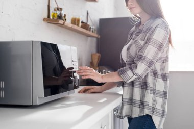 cropped view of woman in shirt using microwave in kitchen 