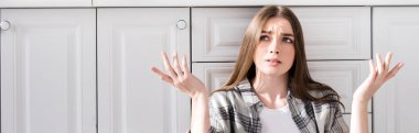 panoramic shot of confused woman doing shrug gesture in kitchen