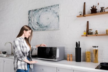 side view of smiling woman looking at microwave in kitchen 