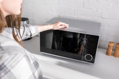 cropped view of woman looking at microwave in kitchen 