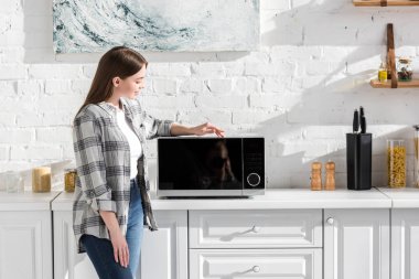 smiling woman in shirt looking at microwave in kitchen 