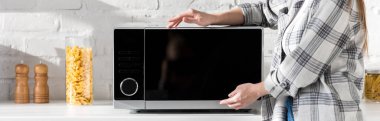 panoramic shot of woman in shirt touching microwave in kitchen  clipart