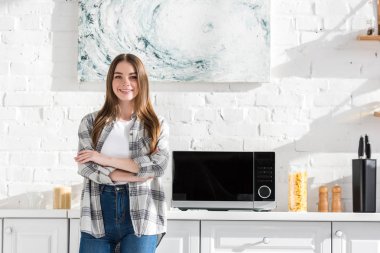 smiling and attractive woman standing near microwave in kitchen 