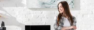 panoramic shot of smiling and attractive woman standing near microwave in kitchen 