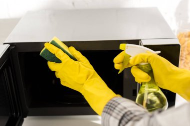 cropped view of woman in rubber gloves cleaning microwave with sponge
