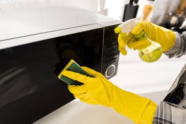 cropped view of woman in rubber gloves cleaning microwave with sponge