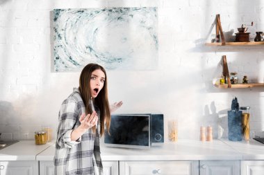 shocked and attractive woman near broken microwave in kitchen 