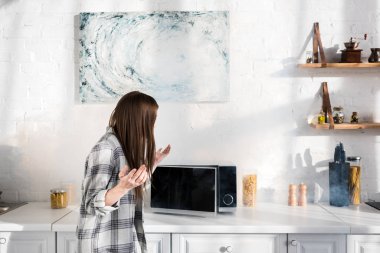 shocked woman looking at broken microwave in kitchen 