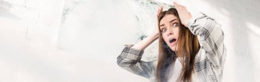panoramic shot of shocked and attractive woman looking away and touching head 