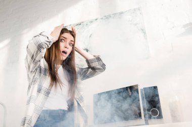 low angle view of shocked and attractive woman near broken microwave in kitchen 