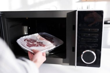 cropped view of woman putting meat into microwave in kitchen  clipart