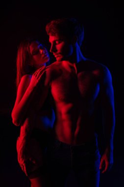 Tutkulu, çıplak, seksi genç çift. Kırmızı ışıkta sarılıyorlar. Siyah ışıkta izole edilmiş.